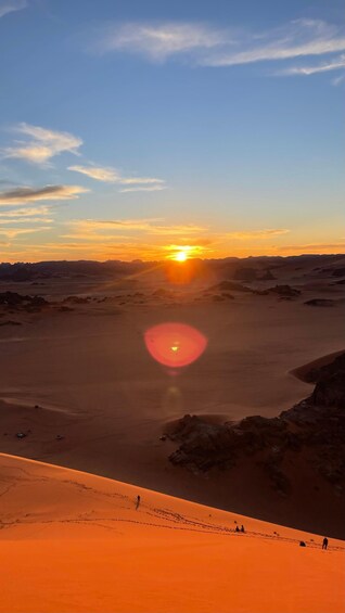 A desert landscape at sunset with a clear sky, distant mountains, and a few people walking. 5