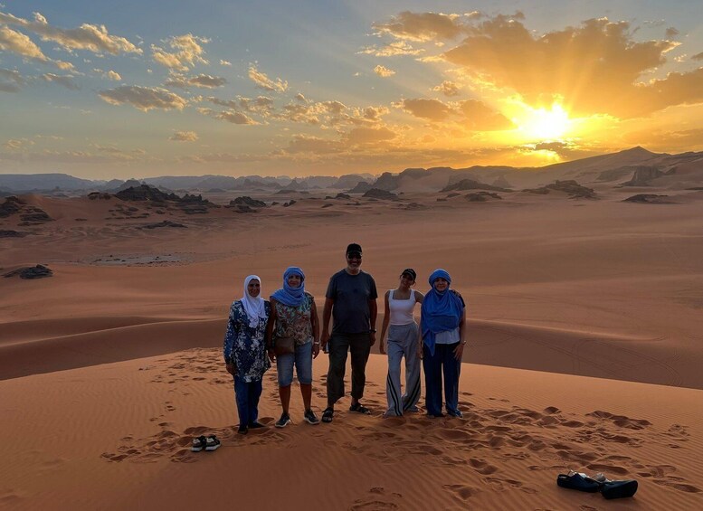 A group of people standing on a sand dune with a sunset in the background. 2
