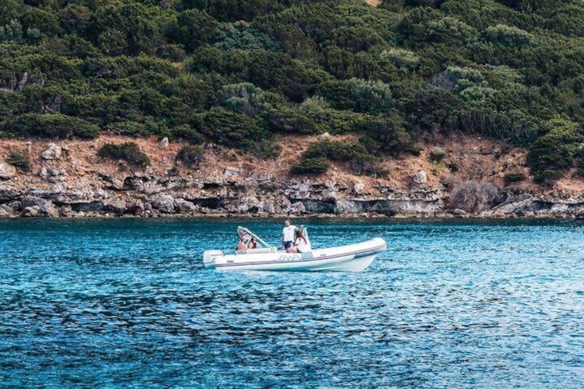 A small boat on calm water with a rocky shoreline and dense greenery in the background. 2