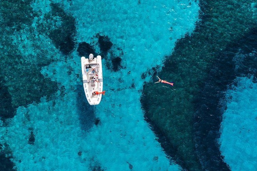 A boat on clear turquoise water with a person swimming nearby. 1