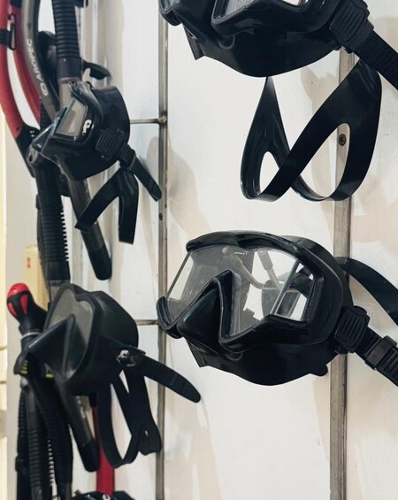 A row of black diving masks with straps, some with red accents, against a tiled wall. 4