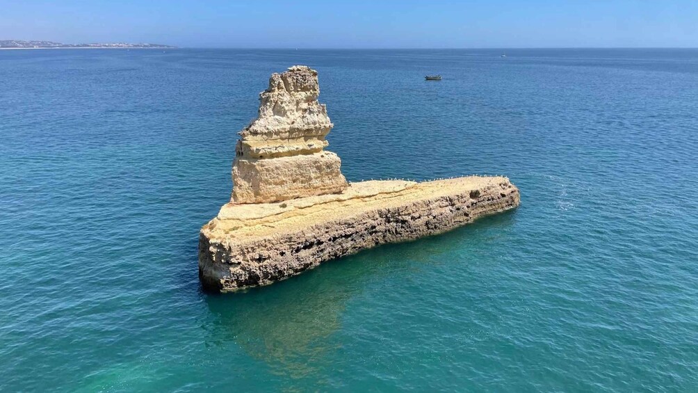 A large rock formation in the sea with a boat in the distance. 3