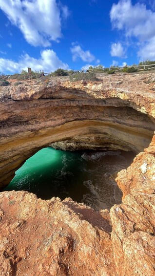 A natural rock arch formation with a turquoise pool beneath it. 5