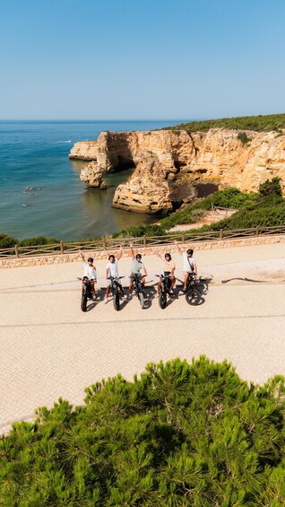 A group of people on bicycles on a paved path by a coastal cliff. 1