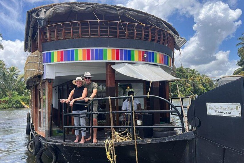 A houseboat with a colorful striped awning, a thatched roof, and a sign indicating it is in Manipur. 1