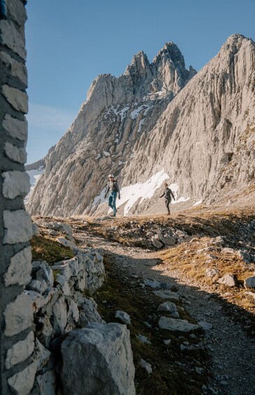 A rocky mountain path with hikers and a stone wall. 2