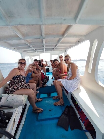 A group of people on a boat with a blue deck, some wearing swimwear, and a clear view of the water. 3