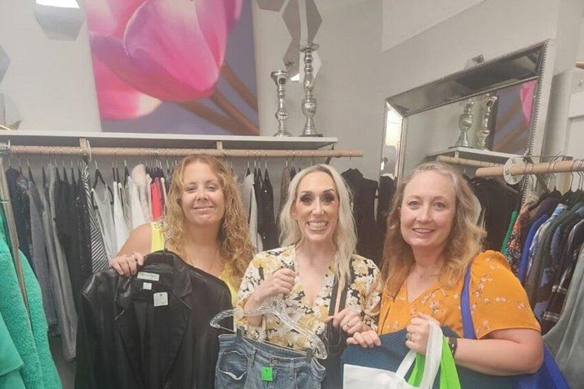 Three people in a clothing store with racks of clothes and a large mirror. 3