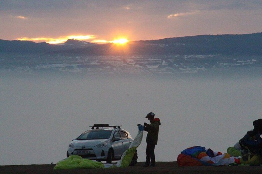 A sunset over a body of water with a car and a person standing nearby. 2