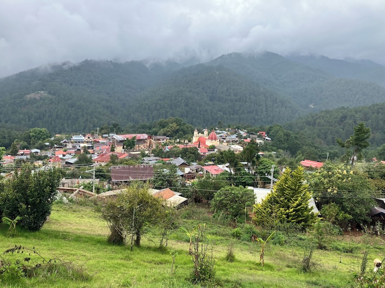 Ein Dorf mit roten Dächern, eine Kirche mit einer roten Kuppel und ein Bergpanorama im Hintergrund. 1