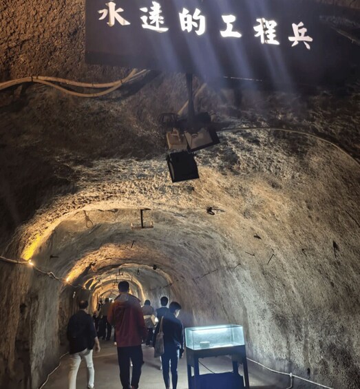 A tunnel with people walking through, illuminated by overhead lights, and a sign with Chinese characters. 5