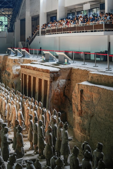 Terracotta soldiers in a museum setting, with visitors observing from an upper level. 4
