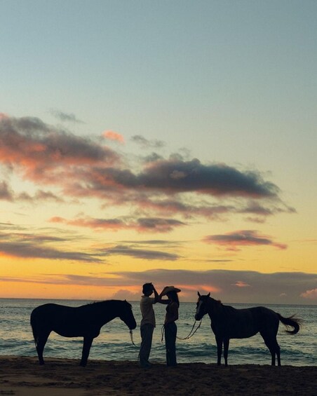 Three people with horses on a beach at sunset. 1