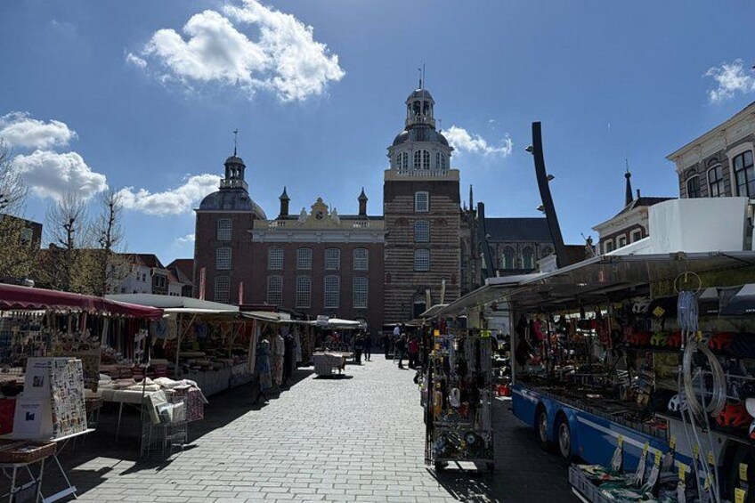 A bustling outdoor market with stalls, a historic building in the background, and a clear blue sky. 4