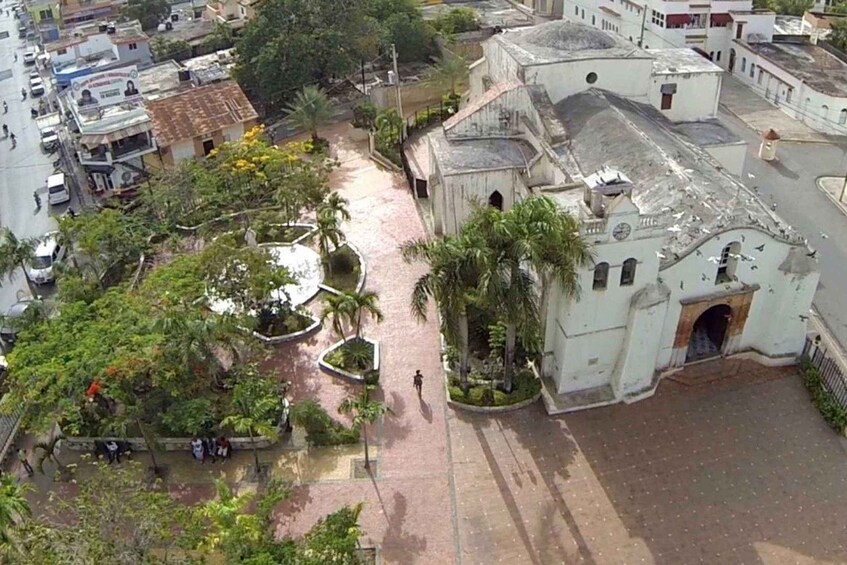 A plaza with a church, palm trees, and surrounding buildings. 2
