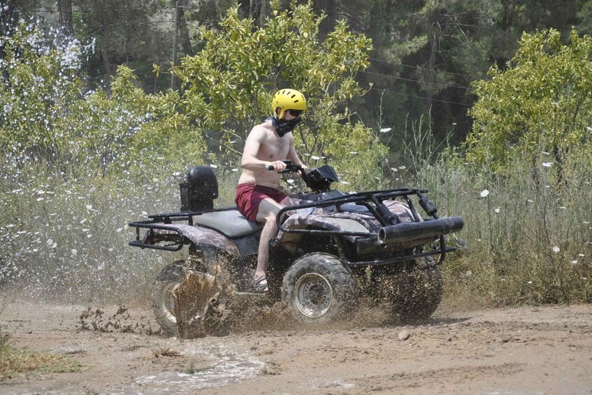 A person riding a four-wheeled vehicle through a muddy area with water splashing around. 3