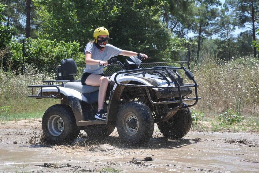 A person riding an ATV on a muddy trail surrounded by greenery. 2