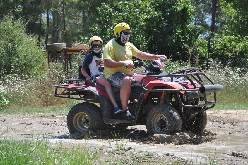 Two people on an ATV in a muddy terrain with trees in the background. 4