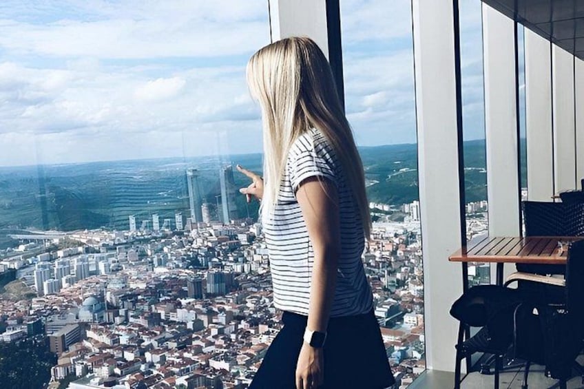 A person standing by a window overlooking a cityscape with buildings and a bridge. 3