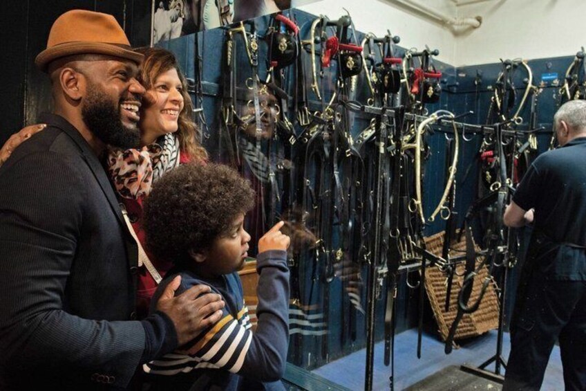 A family observing a collection of equestrian bridles and saddles on display. 3