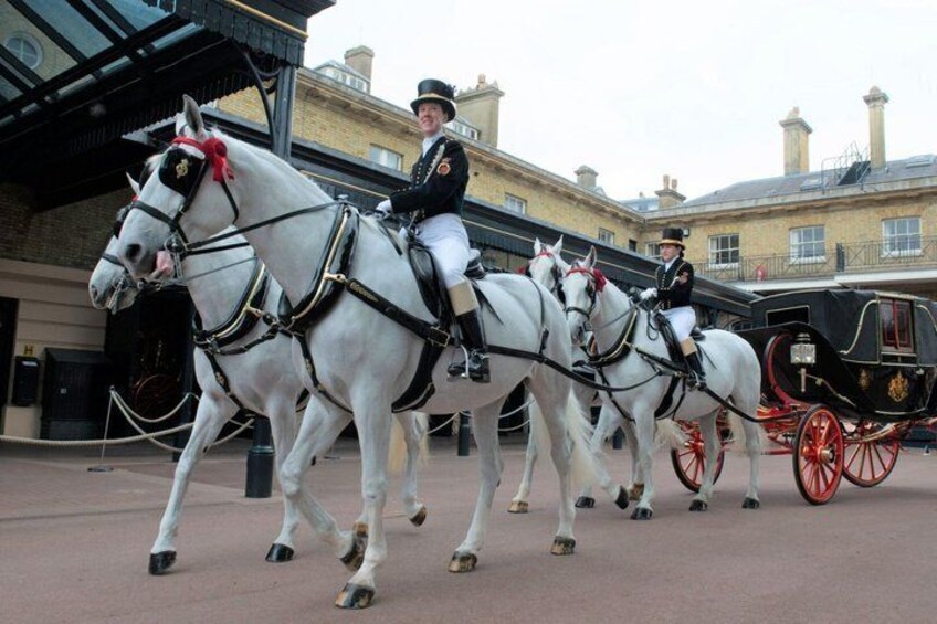 A procession of white horses with riders in formal uniforms, leading a black carriage with red wheels. 4
