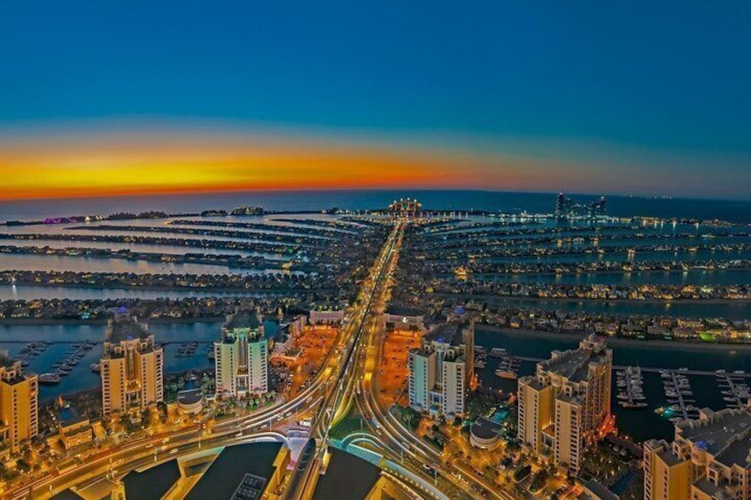 A cityscape at sunset with a prominent highway, high-rise buildings, and a waterfront. 1
