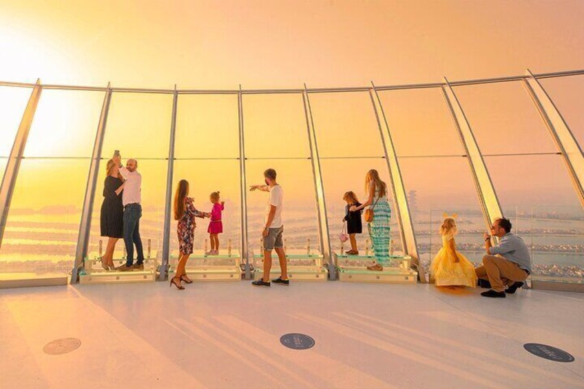 A group of people at a glass observation deck overlooking a cityscape during sunset. 4