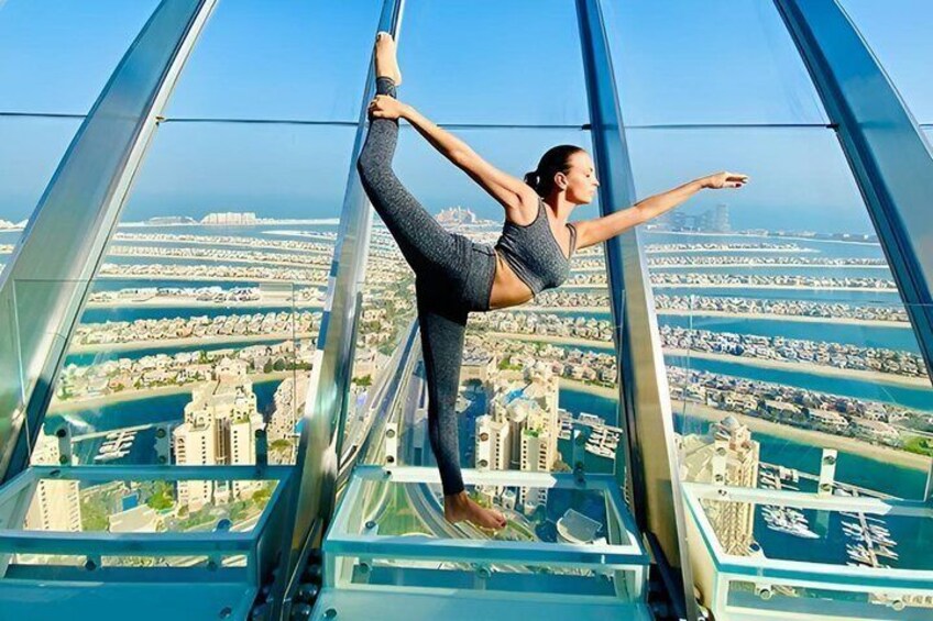 A person performing a balancing act on a glass floor with a cityscape in the background. 3