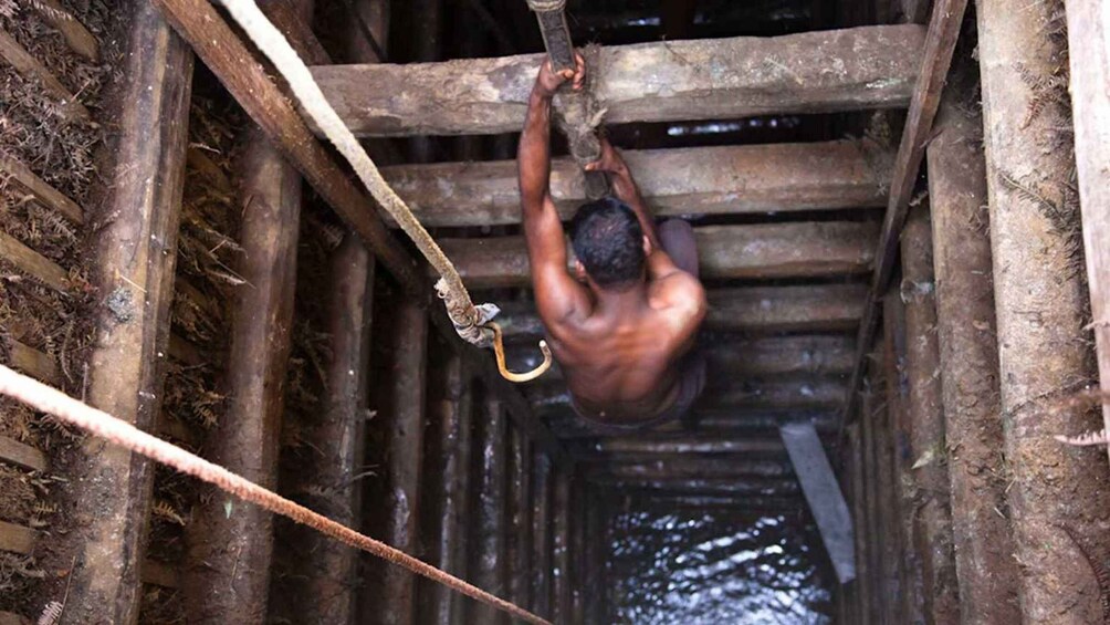 A person hanging from a wooden beam in a narrow, rustic tunnel. 3