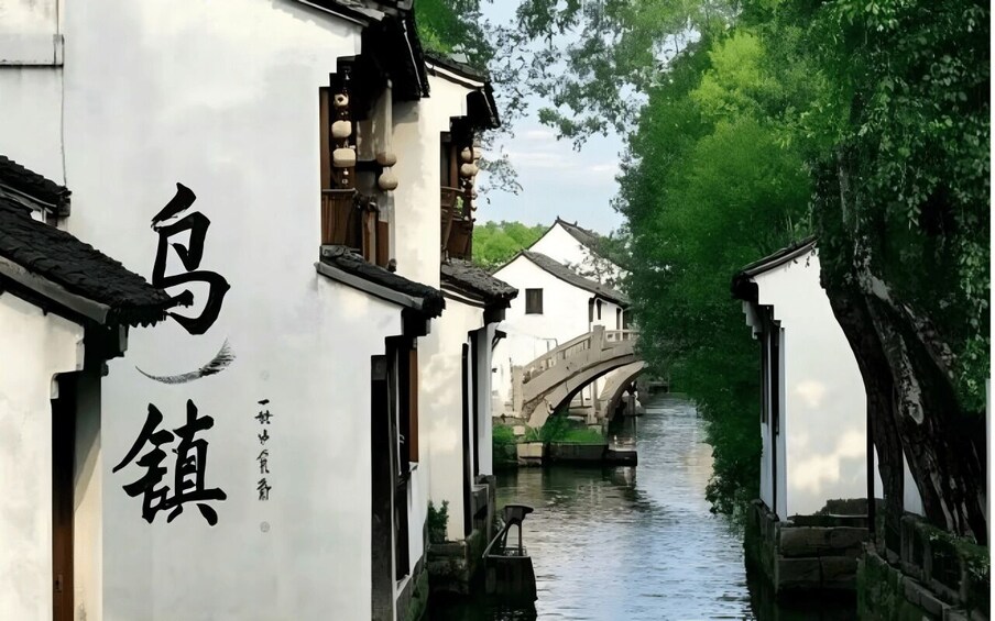 A narrow waterway flanked by traditional buildings with Chinese characters, a stone bridge, and lush greenery. 2
