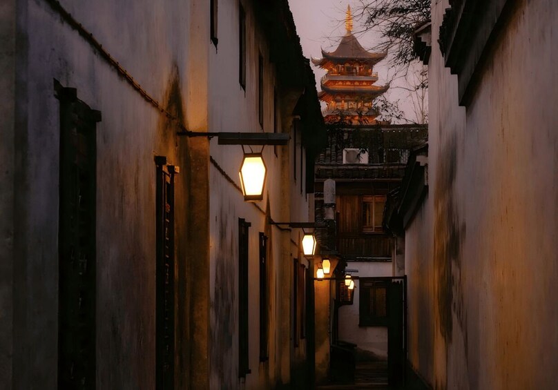 A narrow alleyway with traditional buildings, a pagoda in the distance, and hanging lanterns. 5