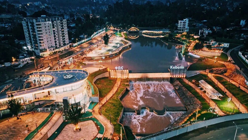 A well-lit urban park with a central water feature, pathways, and surrounding buildings. 5