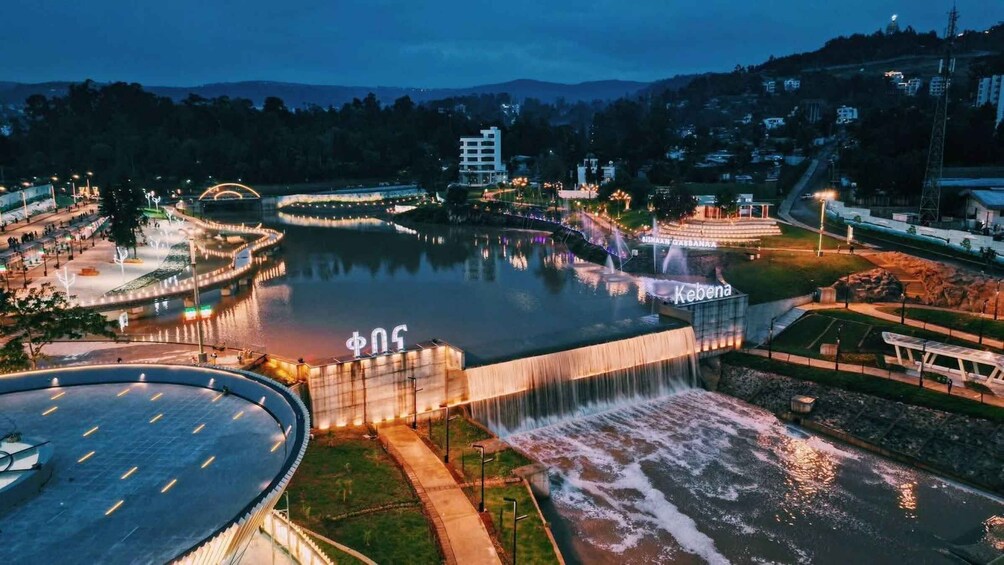 A large water feature with a fountain, surrounded by a park and a bridge, with buildings in the background. 1
