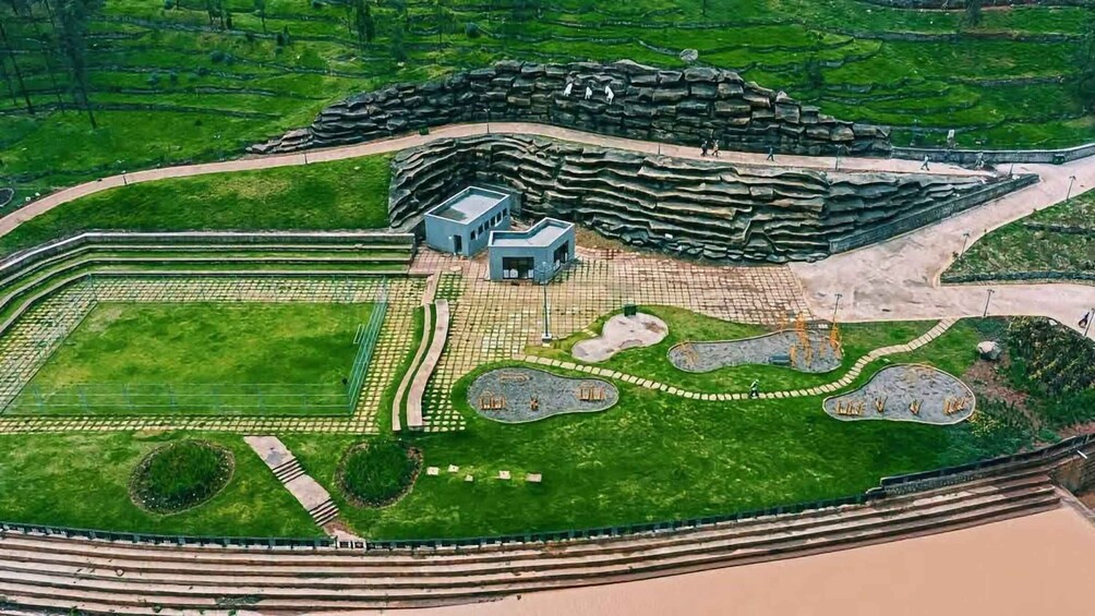 An aerial view of a landscaped area with a large rock formation, pathways, and a few buildings. 3