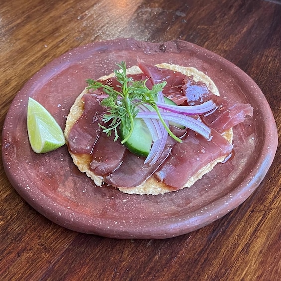 A plate with a slice of meat, a lime wedge, and some green herbs. 1