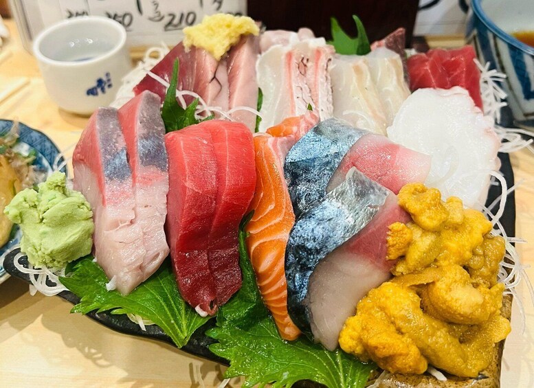 A variety of fresh fish and seafood on a black plate, including sashimi and tempura. 1