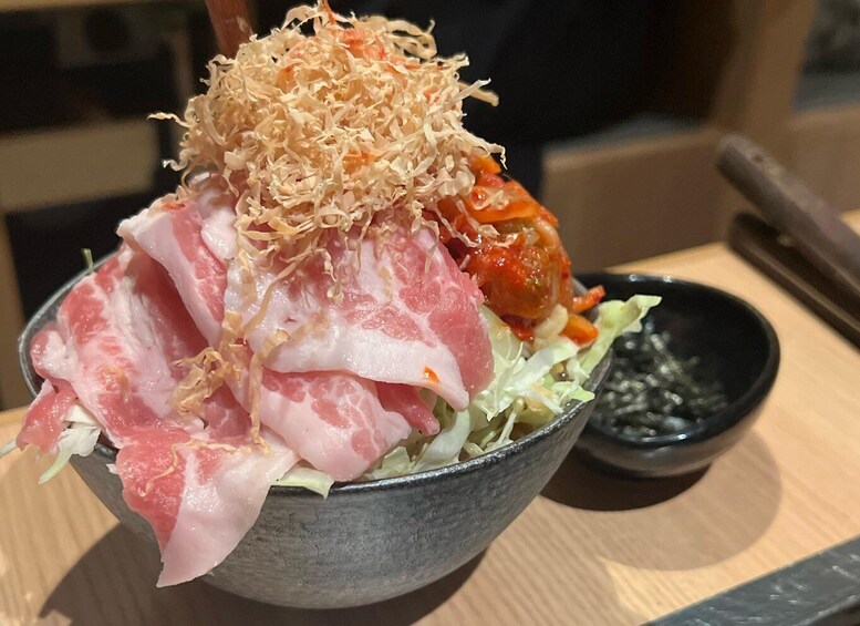 A bowl of sashimi with toppings, including shredded seaweed and a spicy sauce, on a wooden table. 2