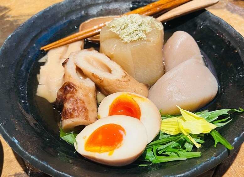 A bowl of Japanese food with various items including a boiled egg, fish, and vegetables. 3