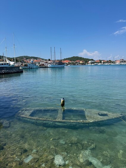 A clear harbor with boats docked, a buoy in the water, and a hilly landscape in the background. 2
