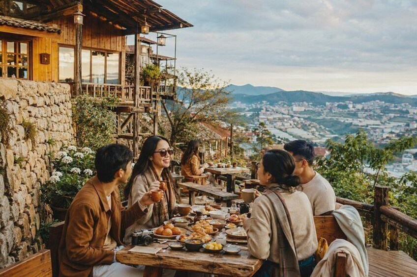 A group of people dining outdoors with a scenic view of a town and mountains in the background. 5
