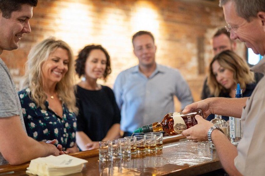A person pouring drinks into shot glasses on a bar counter. 4