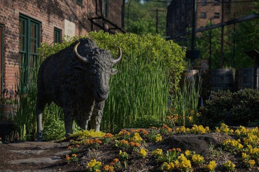 A bull statue in a garden with flowers and a brick building in the background. 5