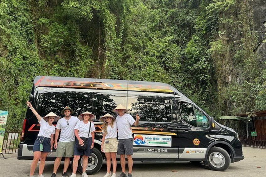 A group of people standing in front of a black bus with a logo and text on the side. 1