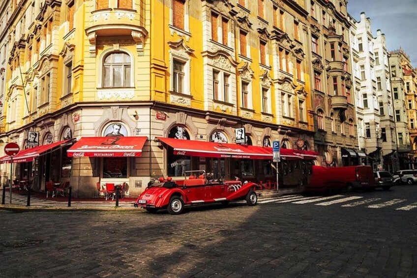 A red vintage car parked in front of a building with ornate architecture and red awnings. 5
