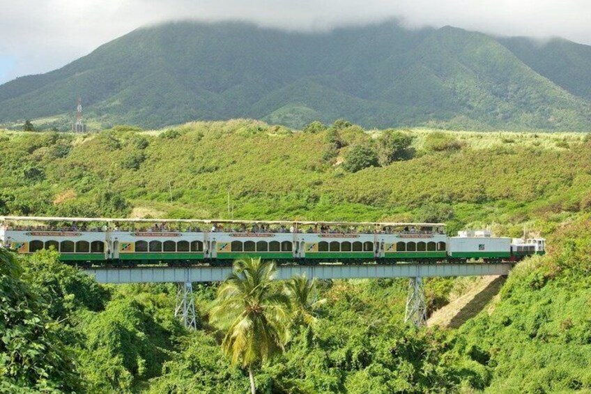A train on a bridge with lush green hills in the background. 4