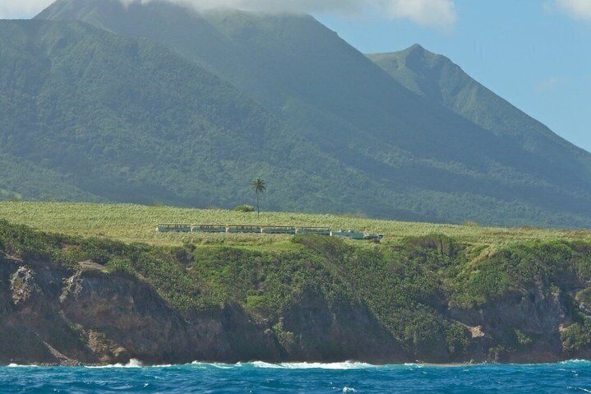 A coastal landscape with a train track, greenery, and a mountain in the background. 3