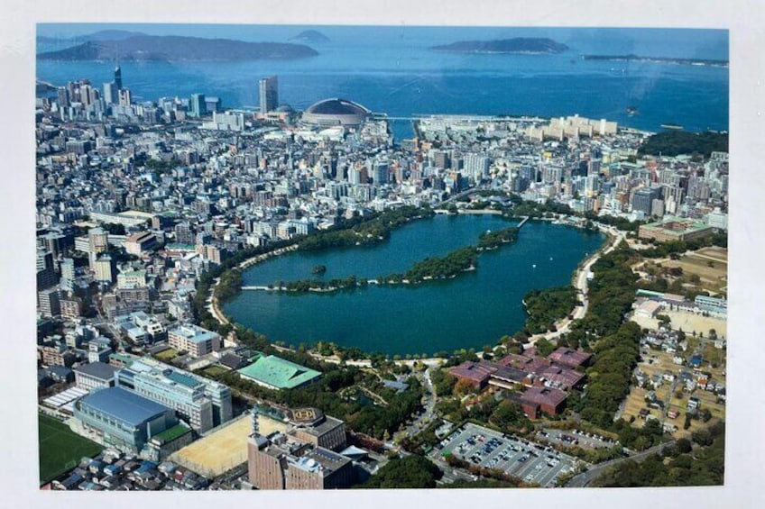 An aerial view of a city with a large body of water, a stadium, and dense urban buildings. 4