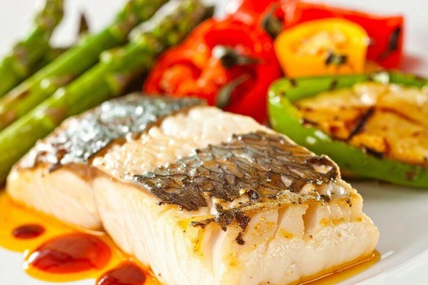 A piece of white fish with a crispy skin, served with grilled vegetables including asparagus, red bell peppers, and a green bell pepper. 2