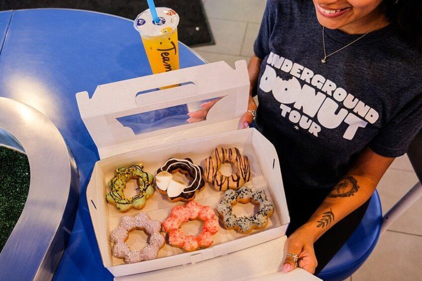 A person holding a box of assorted donuts with various toppings. 5