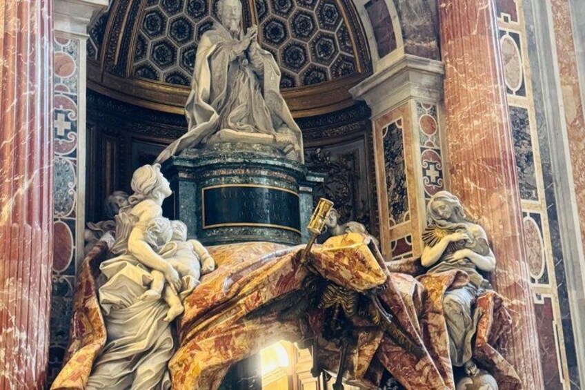 A marble statue of a woman holding a child, surrounded by other figures, in a grand architectural setting with intricate ceiling designs. 4